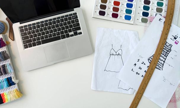 Modedesignerraum. Laptop, Stoffmuster, Farbmusterkatalog für Seidenfäden und Skizzenplatz auf einem großen Tisch. Ansicht von oben - Foto, Bild