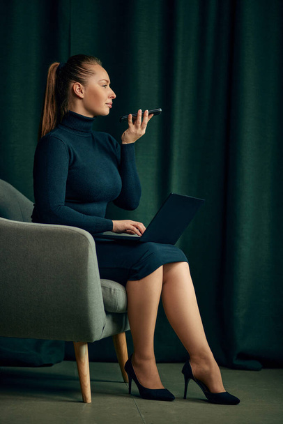 Beautiful, confident, elegant young business woman sitting on chair with laptop and talking on mobile phone. Leading projects, freelance job. Concept of business, fashion, career development - Photo, Image
