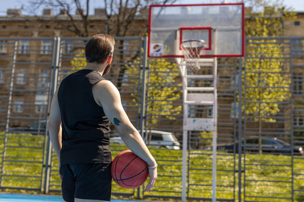 Atlético hombre libanés en ropa deportiva jugando juego de baloncesto, preparándose para lanzar la pelota en el anillo de la cesta. Un joven en la cancha de verano urbana. Rutina de fitness en el campo deportivo. Motivación. Al aire libre - Foto, Imagen