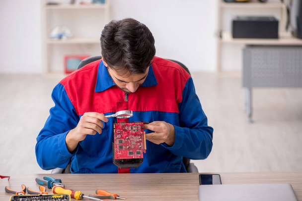 Молодой ремонтник ремонтирует компьютер в лаборатории - Фото, изображение