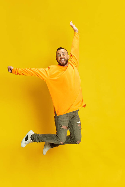 Full-length portrait of excited, happy, smiling bearded man in casual clothes jumping, posing against vivid yellow background. Concept of human emotions, lifestyle, facial expression, sales. Ad - Photo, image