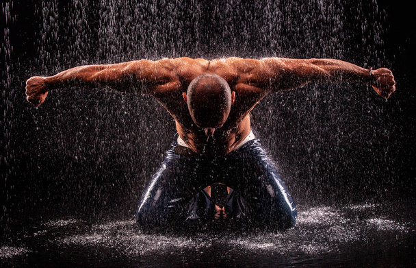 Athlete bodybuilder under jets of rain on a black background - Foto, Imagen