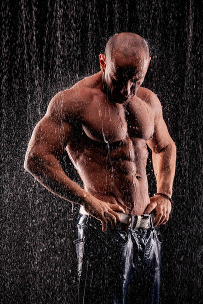 Athlete bodybuilder under jets of rain on a black background - Фото, изображение