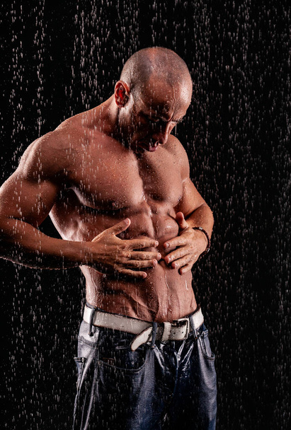 Athlete bodybuilder under jets of rain on a black background - Foto, afbeelding
