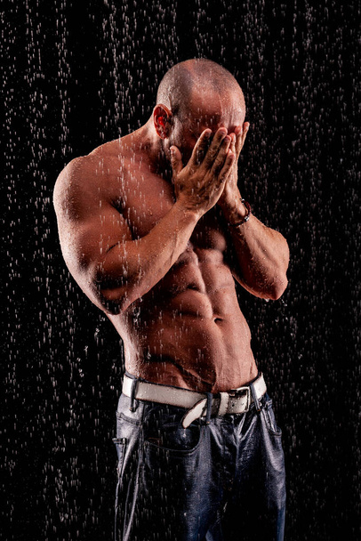 Athlete bodybuilder under jets of rain on a black background - Fotografie, Obrázek