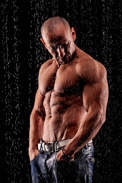 Athlete bodybuilder under jets of rain on a black background - 写真・画像