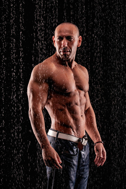 Athlete bodybuilder under jets of rain on a black background - Фото, зображення