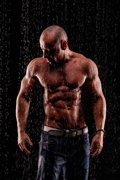 Athlete bodybuilder under jets of rain on a black background - Foto, Imagem