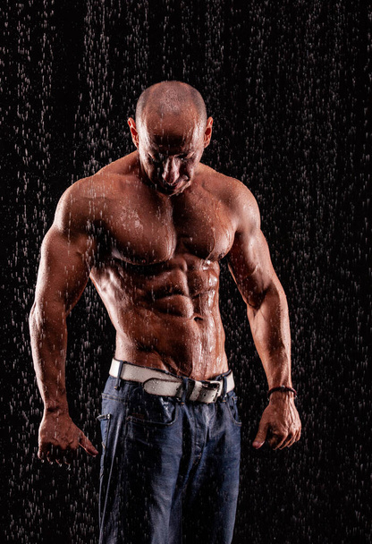 Athlete bodybuilder under jets of rain on a black background - Photo, image