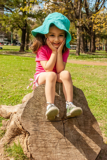 Cheerful little girl sitting on a tree in the park - Fotoğraf, Görsel