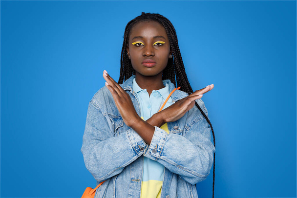 Handgesten. Besorgte junge schwarze Frau in elegantem lässigem Outfit und hellem Make-up mit Stopp-Geste, die Hände auf blauem Studiohintergrund gekreuzt - Foto, Bild