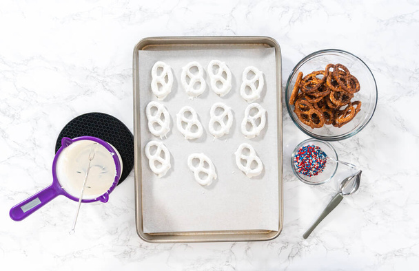 Flat lay. Dipping pretzels twists into melted chocolate to make red, white, and blue chocolate-covered pretzel twists. - 写真・画像