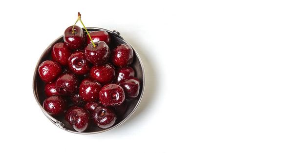 Sweet cherries in a metal bowl on wooden background, closeup. Fresh ripe sweet cherries in a bowl with droplets of water, top view - Photo, image