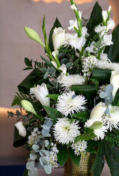 Bouquet of white flowers, chrysanthemums and lilies in glass jar on white table against neutral wall background. Fresh, lush, wedding lily bouquet of colorful flowers, gift on blurred background.  - Photo, Image