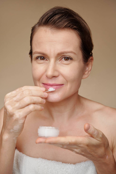 Smiling mature woman applying sugar scrub on lips - Photo, Image