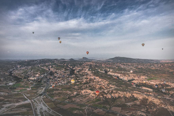 A breathtaking aerial view of a Cappadocia cityscape, on a sunny day, surrounded by beautiful nature, with hot-air balloons flying over the city - Φωτογραφία, εικόνα