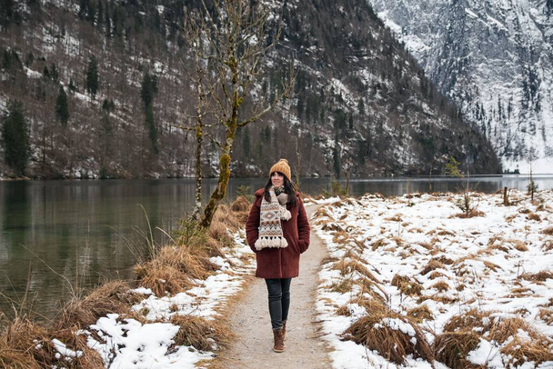 An adventurous girl in a brown coat and scarf walking on a trail at Lake Konigssee in Bavaria, Germany - Foto, afbeelding