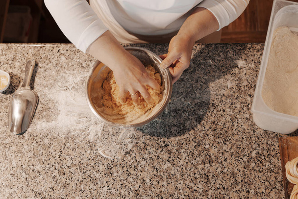 Vue du dessus de la pâte crue de malaxage de cuisinière anonyme de culture dans un bol en métal placé sur le comptoir de marbre lors de la préparation des aliments - Photo, image