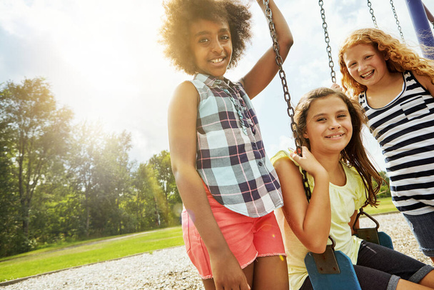Nic poza słońcem i zabawą. Portret młodych dziewczyn bawiących się na huśtawkach w parku - Zdjęcie, obraz