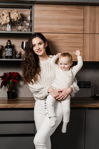 Mother is hugging and kissing her child daughter on the kitchen. Mon and her kid spend time at home together - Zdjęcie, obraz