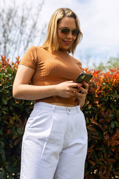 A beautiful shot of a smiling young woman holding her phone  in a park - Foto, imagen