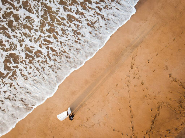 An aerial top view of a bride and groom walking together on a beautiful sandy seashore - Φωτογραφία, εικόνα