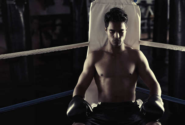 Hes found his place in the boxing ring. Portrait of a young male boxer sitting in a corner of a boxing ring - 写真・画像