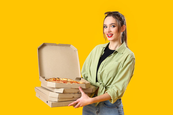 Jonge vrouw met kartonnen dozen lekkere pizza op gele achtergrond - Foto, afbeelding
