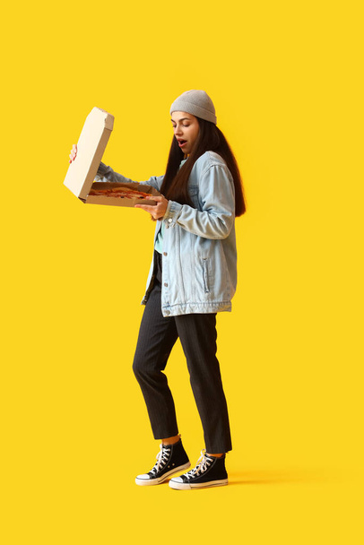 Young woman with box of tasty pizza on yellow background - Фото, зображення