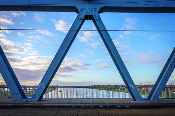 A metal structure of a bridge over a river against blue sky - Fotografie, Obrázek