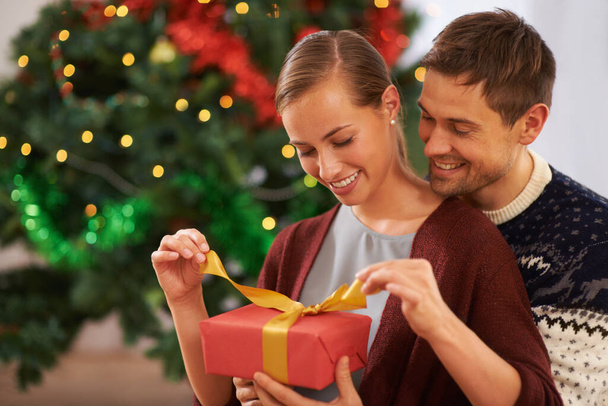 Unwrapping her Christmas guft. an affectionate young couple on Christmas day - Photo, Image