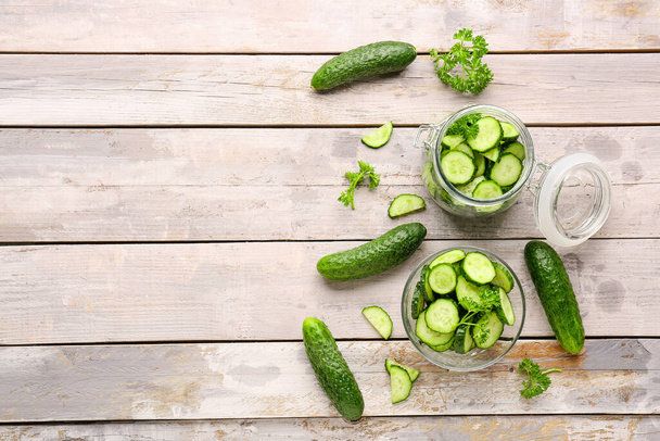 Jar and bowl with fresh cut cucumbers on light wooden background - Photo, Image