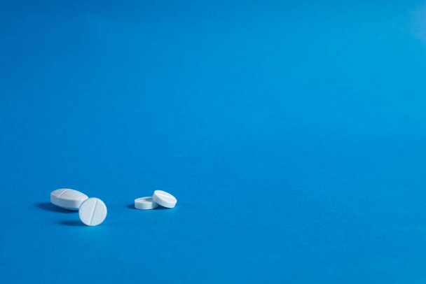 Round white pills, close-up on a blue background. Copy space. Background image on medical and pharmaceutical subjects - Fotoğraf, Görsel