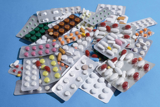 A large pile of pills in bundles scattered on the table. A mound of multi-colored tablets and blister packs. Close-up, copy space - Zdjęcie, obraz