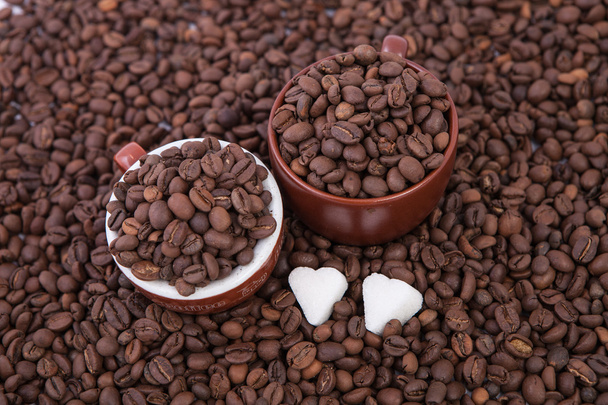 Δύο φλιτζάνια του καφέ, γεμάτο από ψημένα φασόλια καφέ και 2 κομμάτια ζάχαρης καρδιά - Φωτογραφία, εικόνα