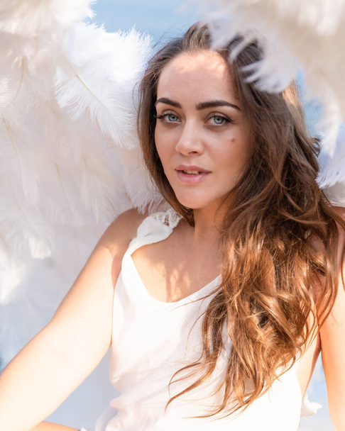 Close portrait of a young woman. Blue-eyed girl with white wings is watching us. White angel. Beautiful lady - Foto, imagen