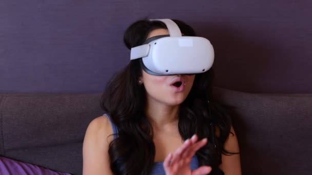 Jolie femme effrayée utilisant un casque VR, regardant vers le haut dans la réalité virtuelle, assise sur le lit à sa maison. Concept de technologie moderne. Mouvement lent - Séquence, vidéo