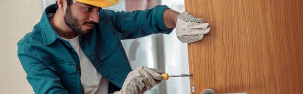 Trabajador de cerrajería en uniforme instalando pomo de puerta. Servicio de reparación profesional. Concepto de mantenimiento - Foto, imagen