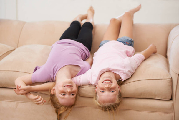 Spending time with a friend. Two young girls lying upside down on a couch - Фото, изображение