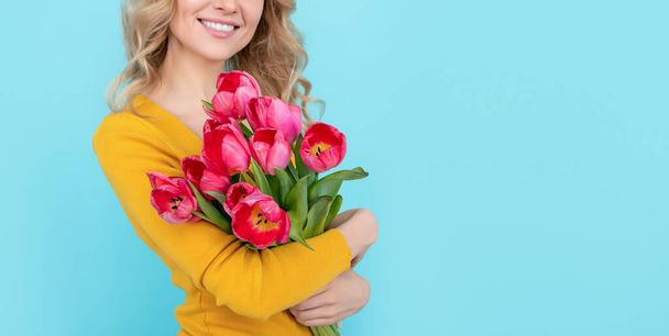 positive young woman with spring tulip flowers on blue background. womens day. - Photo, Image