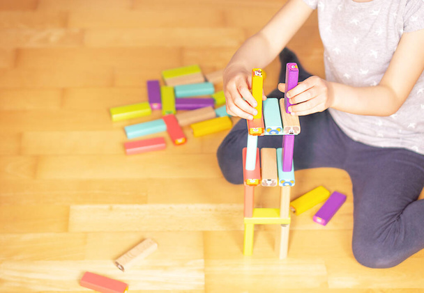 Kind zittend op de grond in de flat en spelend met kleurrijke speelgoedblokken. Speelgoedhuis voor kinderen. Hoge kwaliteit foto - Foto, afbeelding