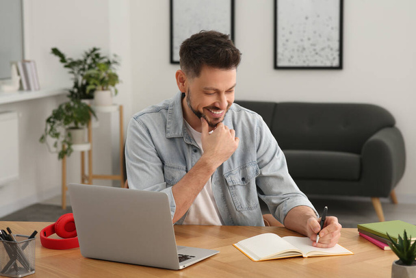 Online translation course. Man writing near laptop at home - Фото, изображение