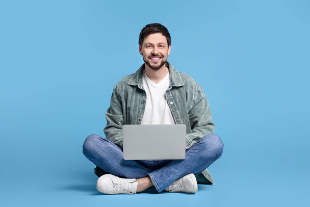 Happy man with laptop on light blue background - Fotoğraf, Görsel