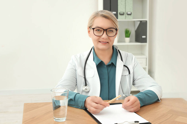 Professional doctor sitting at wooden table in clinic - Foto, Bild