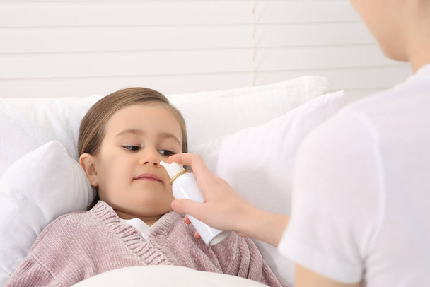 Mother using nasal spray to treat her little daughter on bed - Foto, immagini