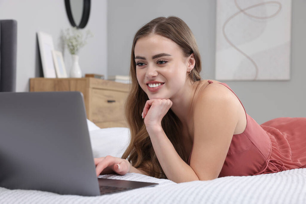 Happy woman with laptop on bed in bedroom - Photo, Image