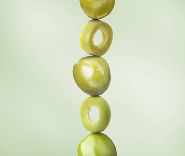 Cut and whole olives on dusty light green background - Fotoğraf, Görsel