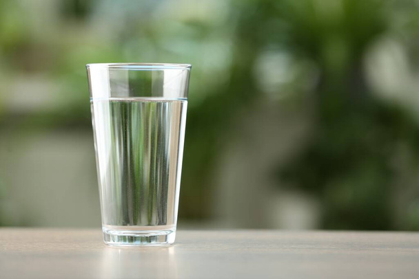 Glass of water on white table against blurred green background, closeup. Space for text - Photo, image