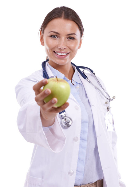 Giving the gift of good health. Portrait of a beautiful young doctore holding out an apple and smiling against a white background - Foto, Imagem