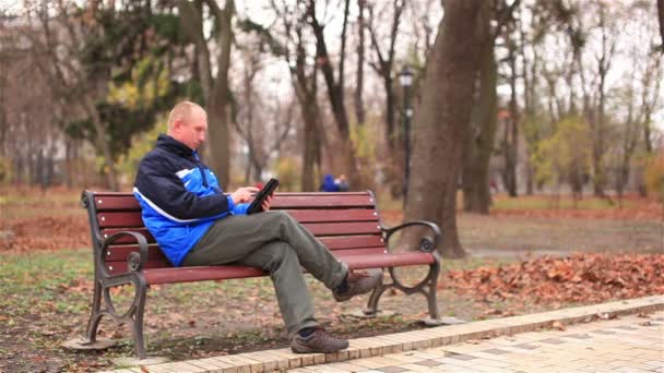 Взрослый мужчина работает над планшетом в парке
 - Кадры, видео